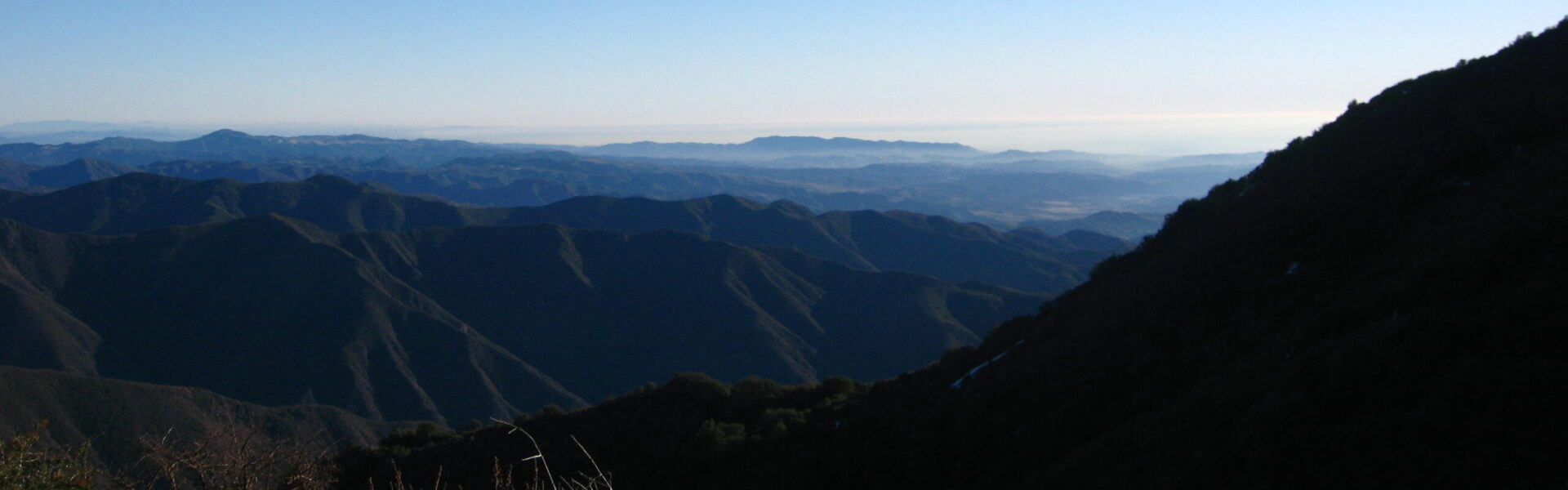 Dimly lit elevated view of a mountain range cascading down to a city valley with a hazy blue sky