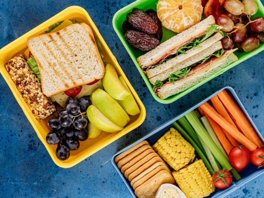 Three colored lunch trays with a variety of sandwiches, fruits, vegetables and snacks