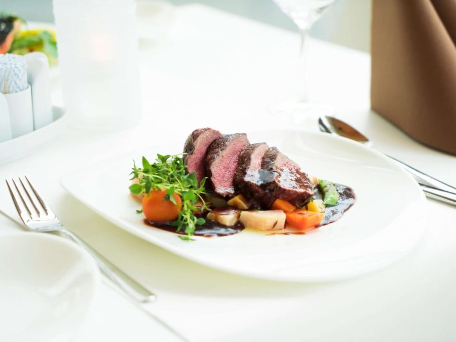 A medium cooked sliced steak and vegetables on a white plate and tablecloth