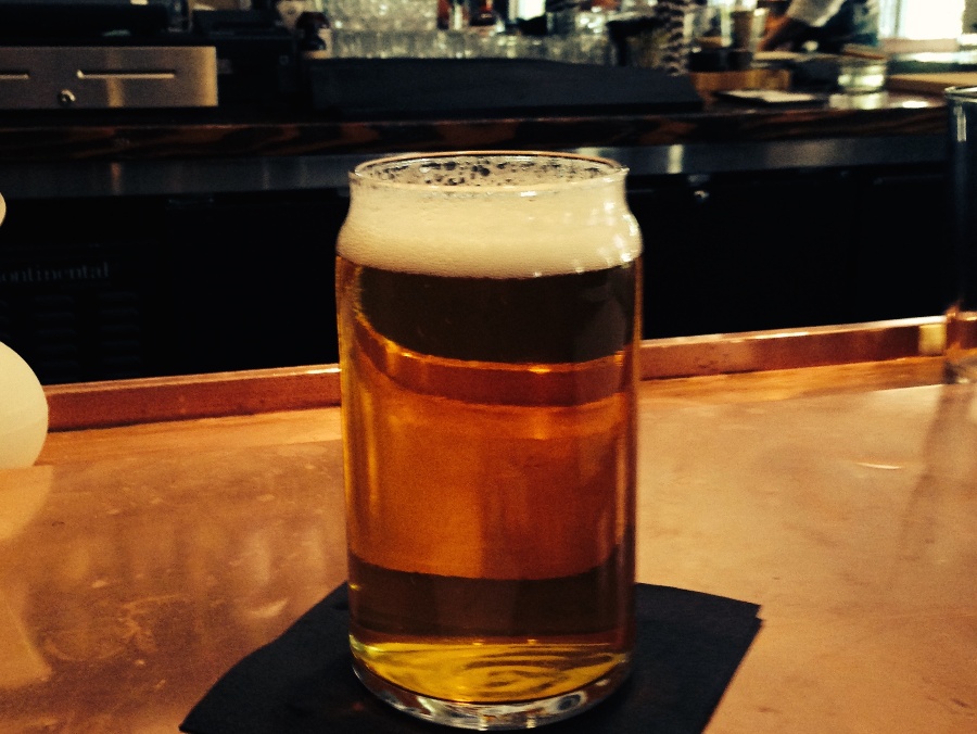 A pint of amber beer with a white foam head on a metal bar counter. Link to Where to Find a Drink on page