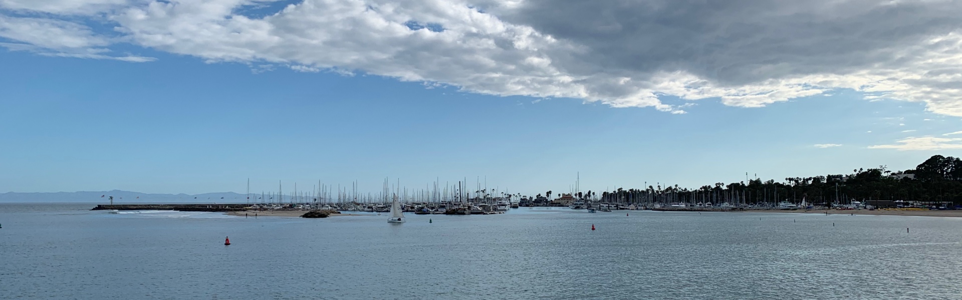 Panoramic view of ocean, sail boats, shoreline, blue sky and a curtain of clouds above