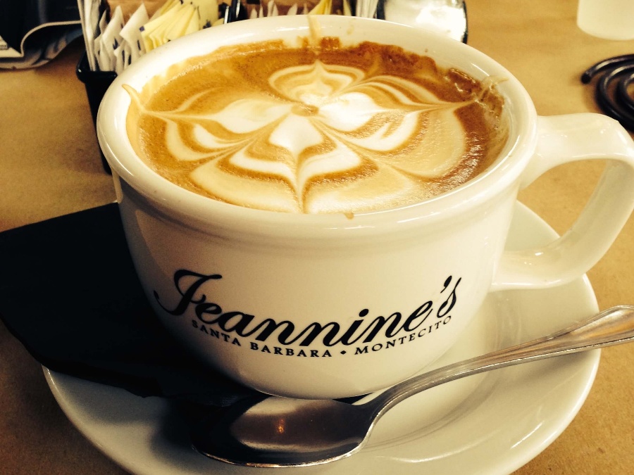 Full cup of Latte coffee with flower Latte art on the surface. Latte in a white mug on a saucer with a spoon resting on it