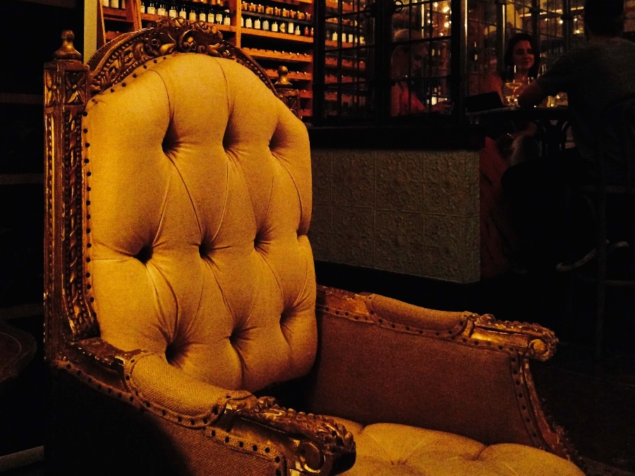 Empty tufted burnt yellow chair with ornate wood frame in the dimly lit Lark restaurant in Santa Barbara