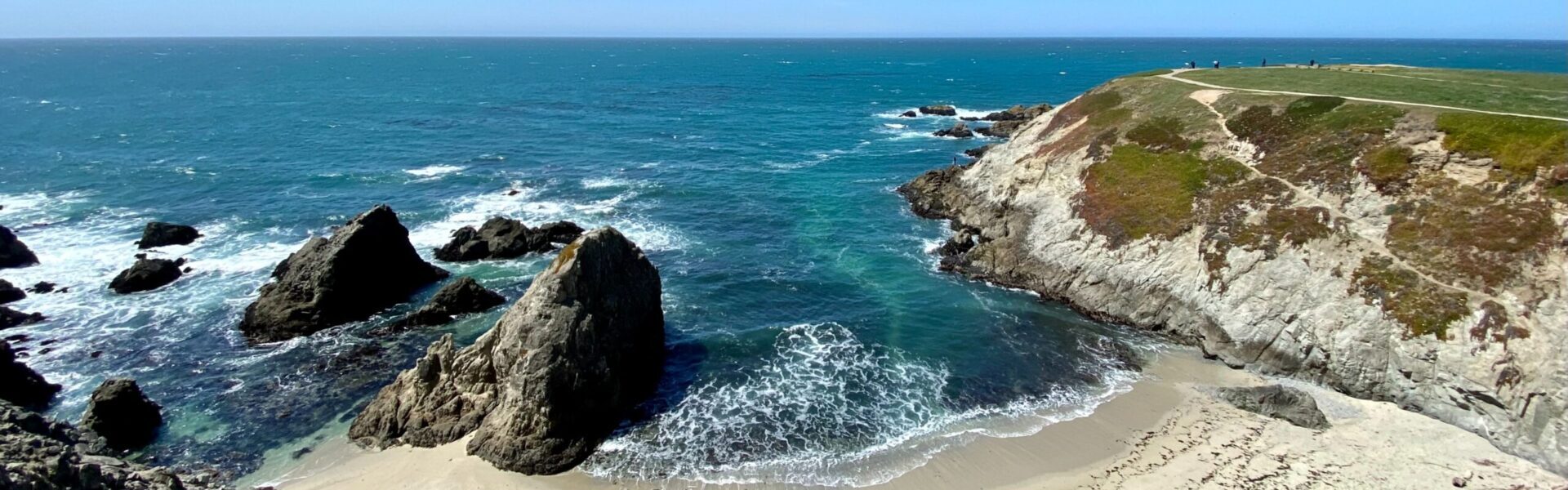 Elevated view of sandy beach cove surround by cliffs and water crashing on rocks