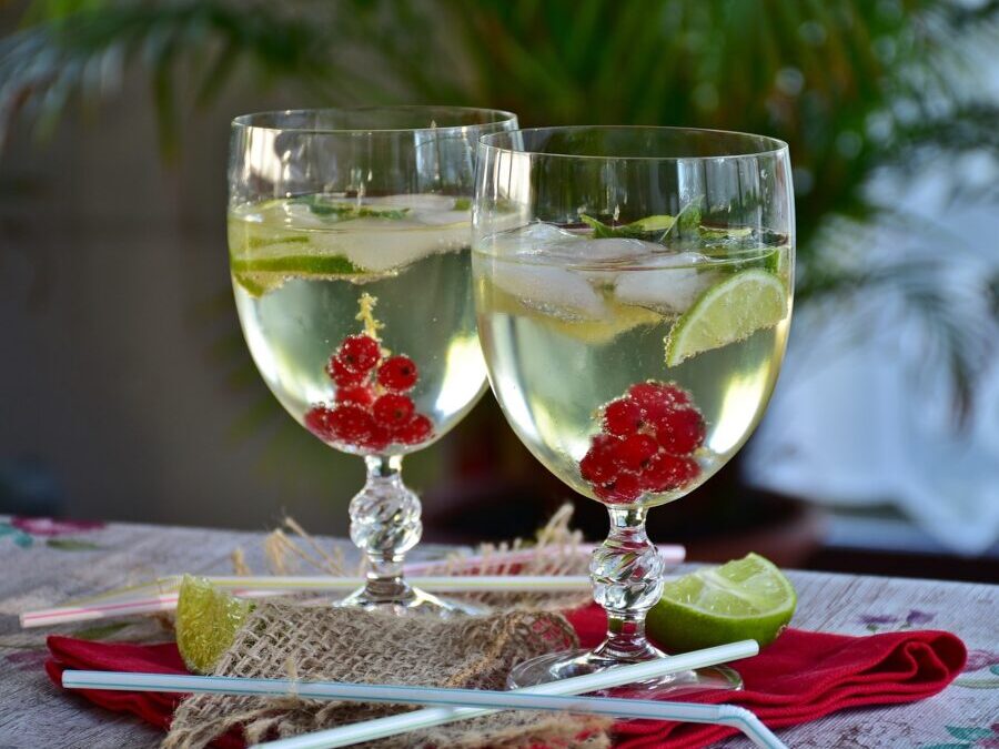 Two Prosecco cocktails with lime, and berries in clear glasses. Plastic straws, lime wedge, and napkin resting beside them