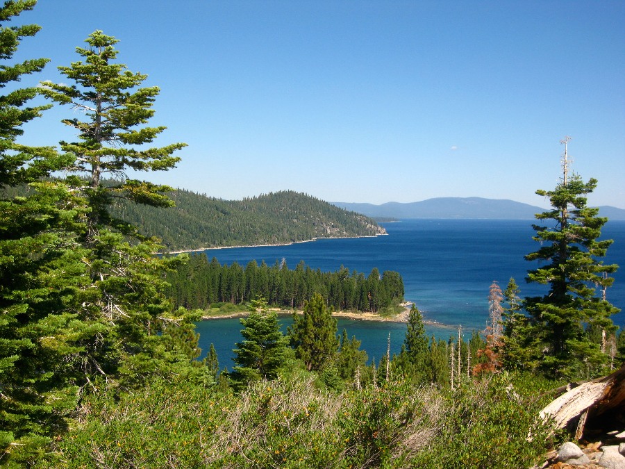 Lush green greens and hills surrounding the deep blue Lake Tahoe with a clear blue sky. Link to Lake Tahoe page.