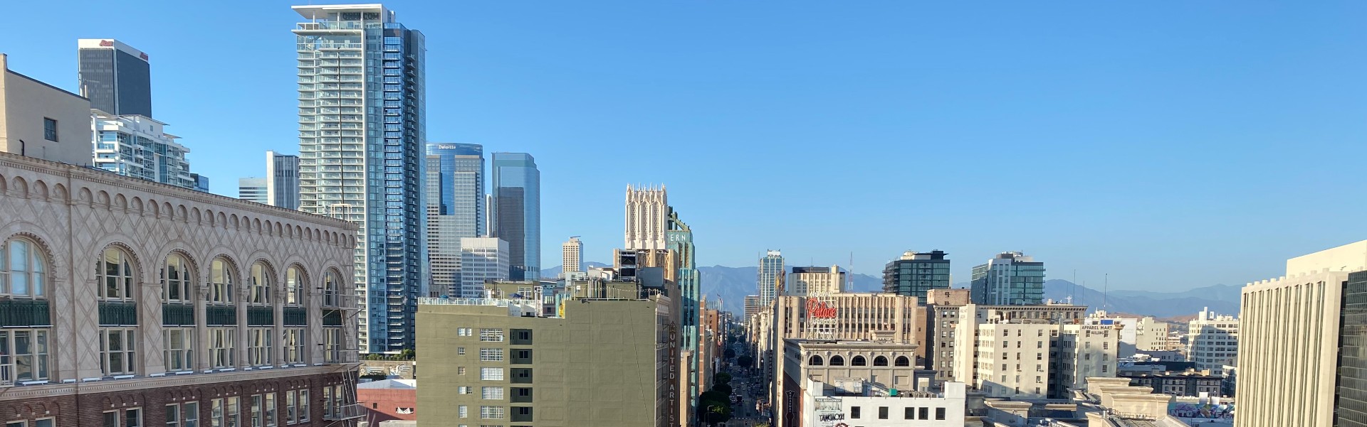 Elevated view of Broadway Street lined with historic buildings in Los Angeles. Clear blue sky and hills in background.