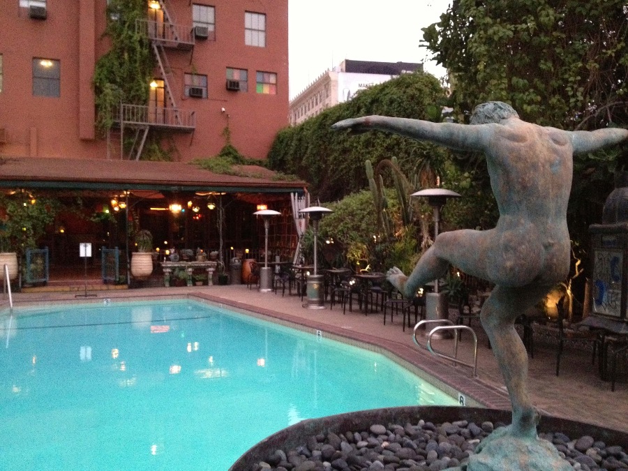 Back view nude male statue in front of hotel pool surrounded by plants and tables. Link to Where to Stay on page.