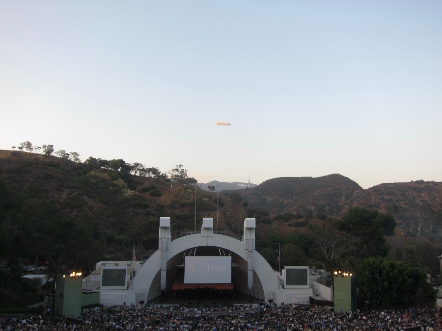 Elevated view of inside the Hollywood Bowl with the Hollywood sign on the background hills and the Goodyear blimp in the sky