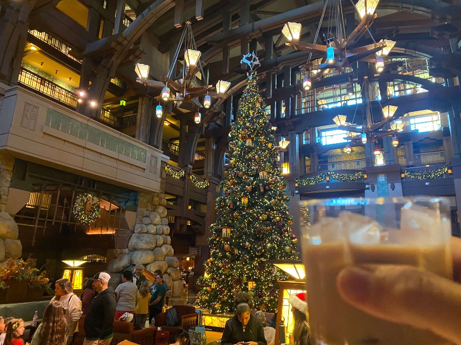 Toasting a drink at Disney Grand Californian Hotel with high wood beams, fireplace, 50-foot tall decorated Christmas tree.