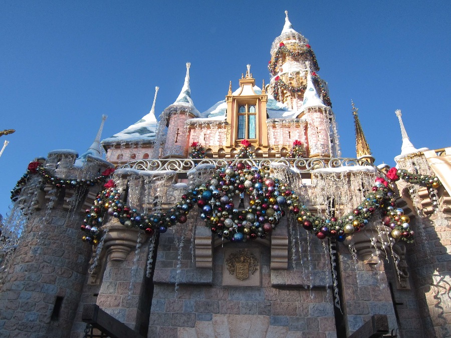 Upward front view of Disneyland Sleeping Beauty Castle with a Christmas wreath, garland, and ornaments.