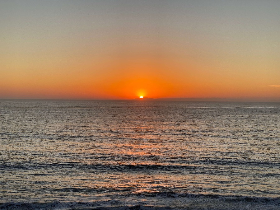 Deep blue ocean at sunset with glowing orange sun and sky setting over the silhouette of Catalina Island.