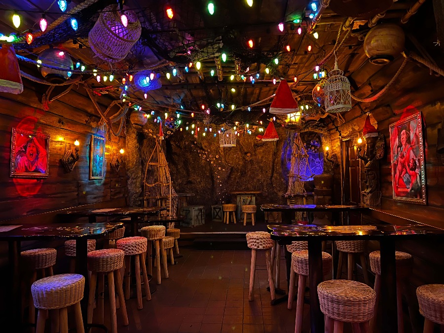 Dim bar with cave and wooden ship-like walls, Christmas lights and the Goonies movie decor.