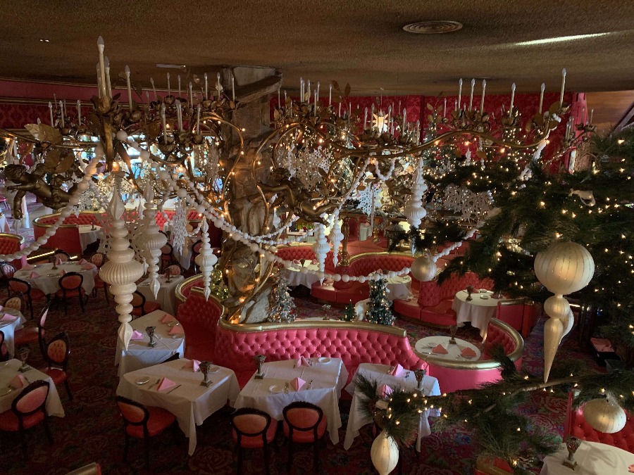 Elaborately decorated Madonna Inn dining room with candles, Christmas garland, decorative snowflakes, and pink booths.