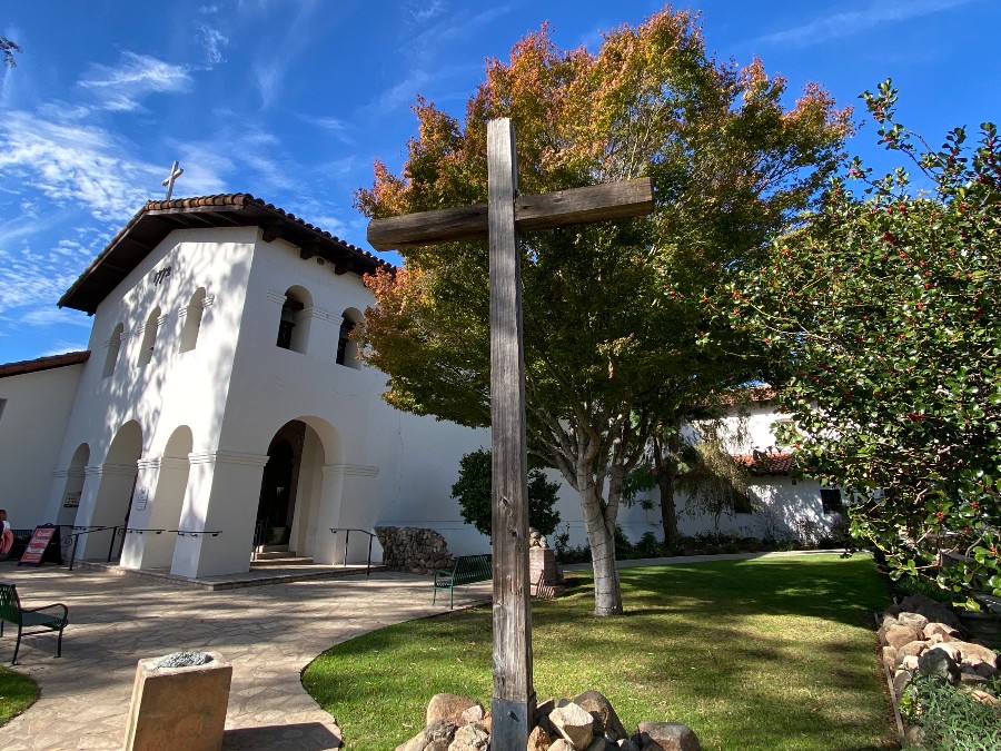 Wooden cross in foreground of the white San Luis Obispo Mission front courtyard. Link to San Luis Obispo page.