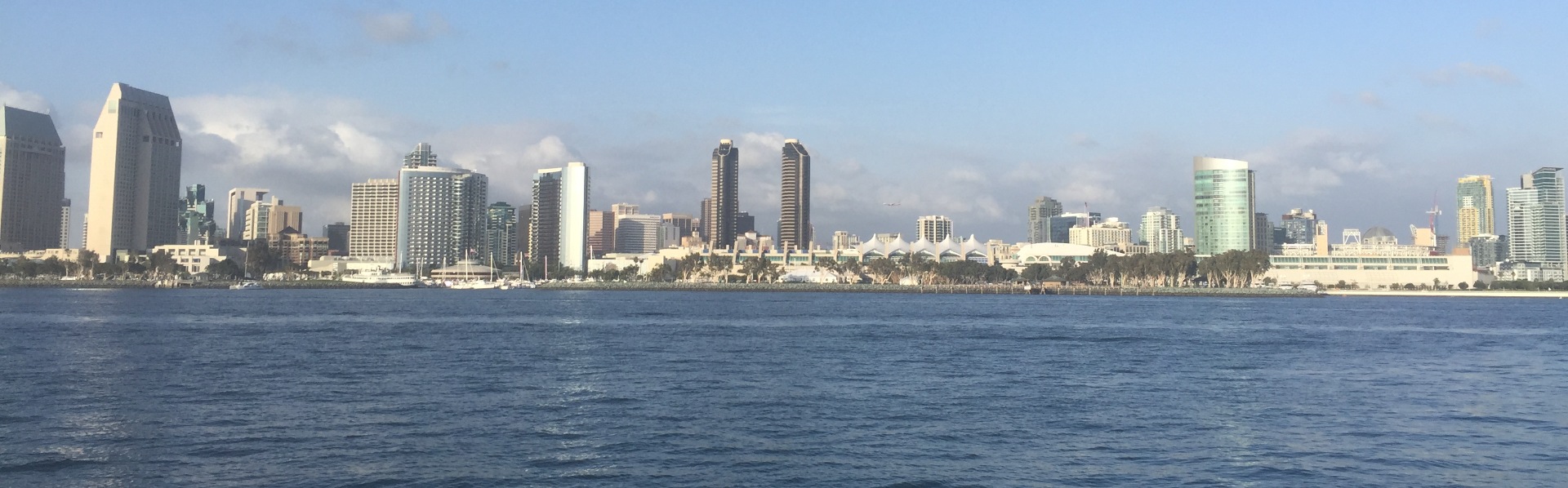 Blue ocean water with San Diego building skyline behind and light blue sky with scattered clouds.