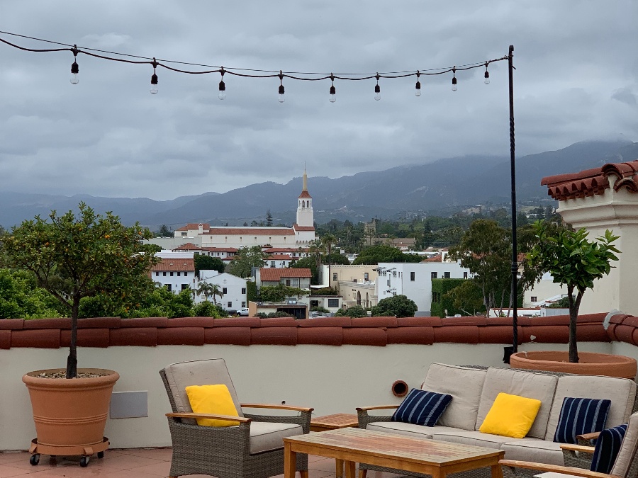 Roof patio lounge with hanging lights with city, hill view of Santa Barbara in the background. Link to Santa Barbara page.