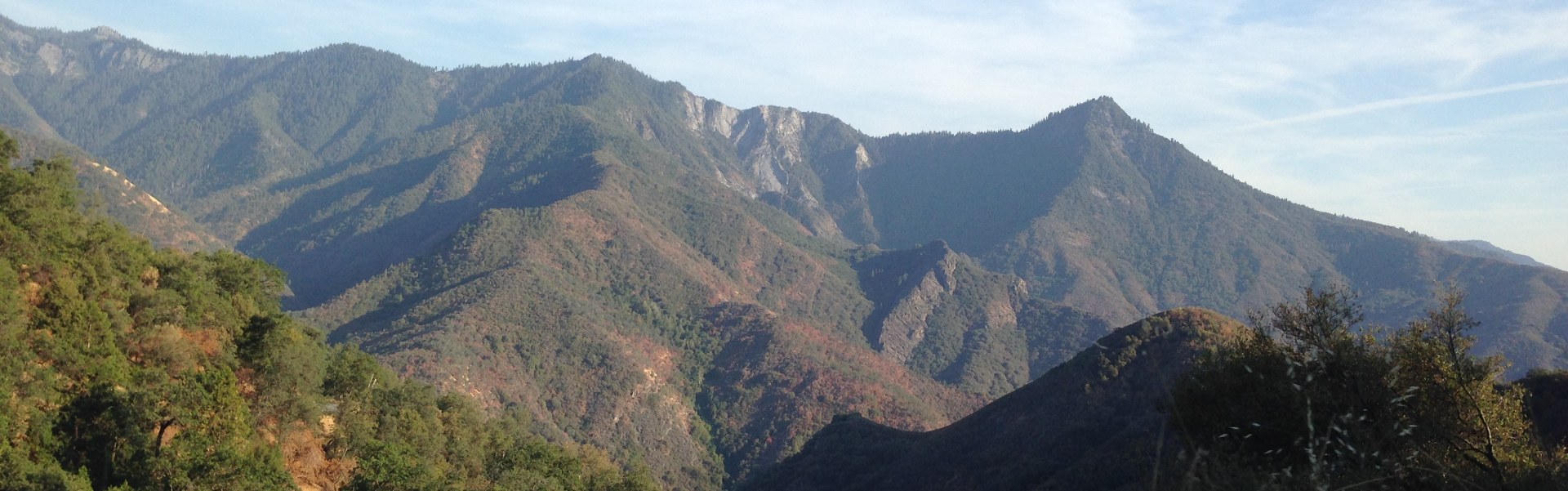 Green and beige mountain range of Sequoia National Park with faint blue sky behind a thin drape of clouds.